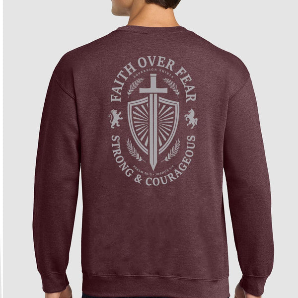 A man wearing a heathered maroon crewneck sweatshirt, viewed from the back. The sweatshirt features a large light gray graphic print on the back with a shield, sword, lions, and the text 'FAITH OVER FEAR' and 'STRONG & COURAGEOUS'.